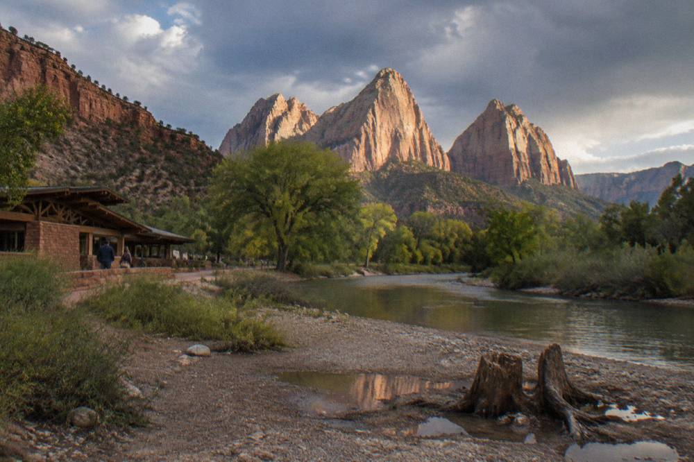 Three tall red sandstone towers rising above green trees along a river bend
